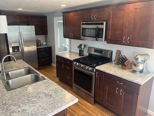 kitchen featuring light wood-style flooring, a sink, stainless steel appliances, decorative backsplash, and baseboards