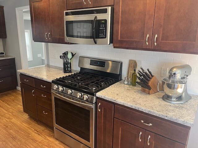 kitchen with light wood-type flooring, stainless steel appliances, light stone countertops, and backsplash