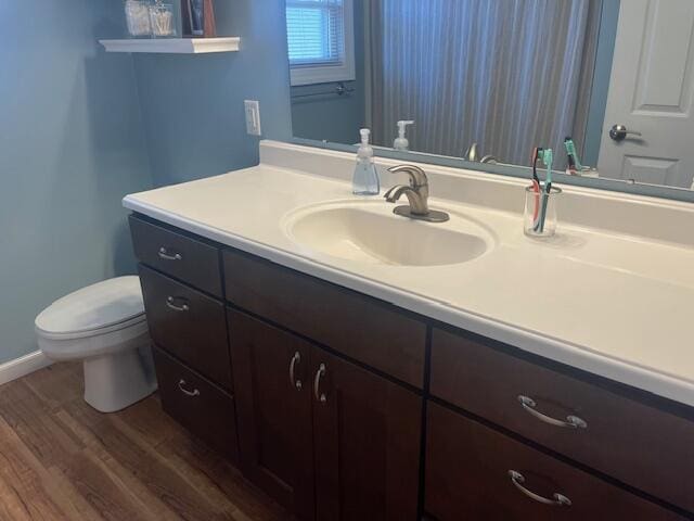 bathroom with toilet, vanity, baseboards, and wood finished floors