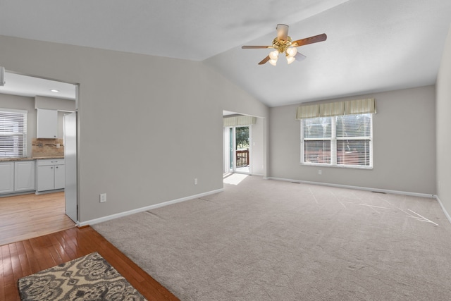 unfurnished living room featuring light wood finished floors, baseboards, a ceiling fan, and vaulted ceiling