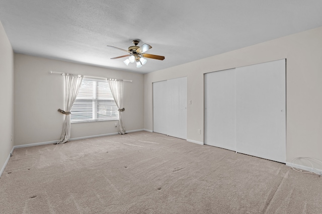 unfurnished bedroom with a ceiling fan, multiple closets, carpet floors, and baseboards