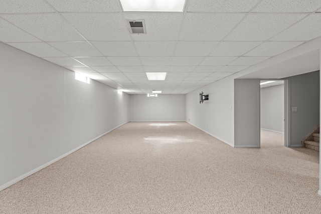 finished below grade area featuring a drop ceiling, baseboards, visible vents, and carpet floors