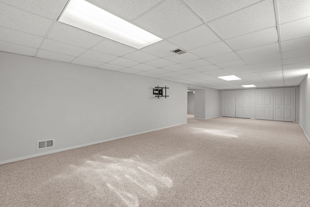 finished basement with light colored carpet, baseboards, visible vents, and a paneled ceiling