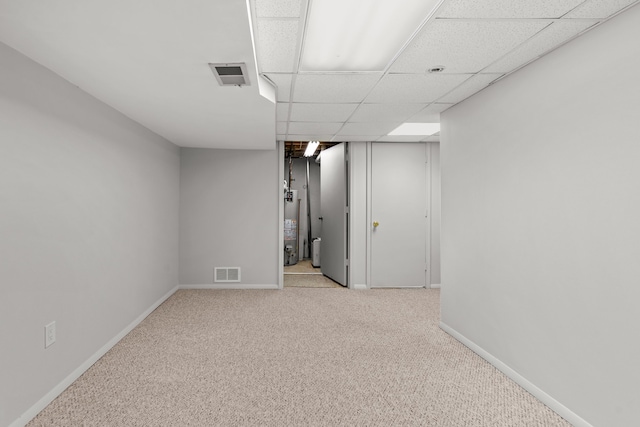 finished below grade area featuring carpet flooring, baseboards, visible vents, and water heater