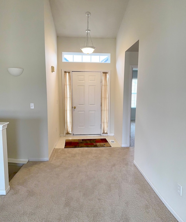 carpeted entryway featuring baseboards, a healthy amount of sunlight, and a towering ceiling