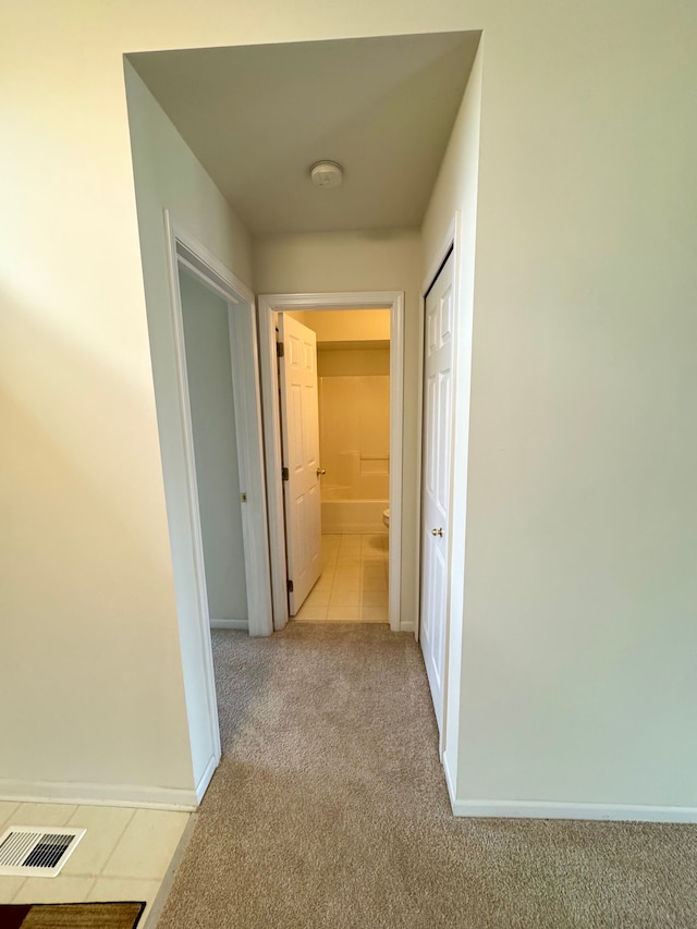 hall featuring baseboards, visible vents, and light carpet