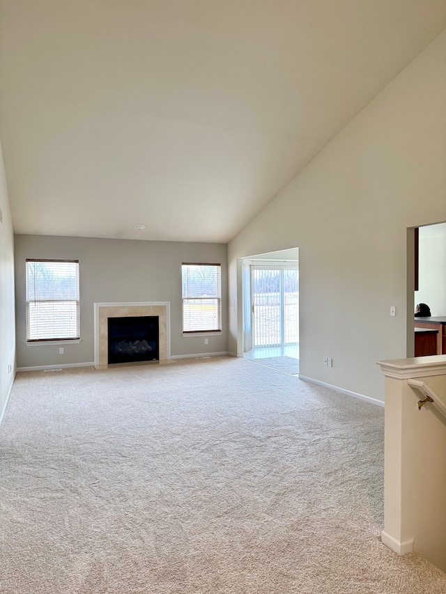 unfurnished living room featuring baseboards, light colored carpet, high vaulted ceiling, and a tile fireplace