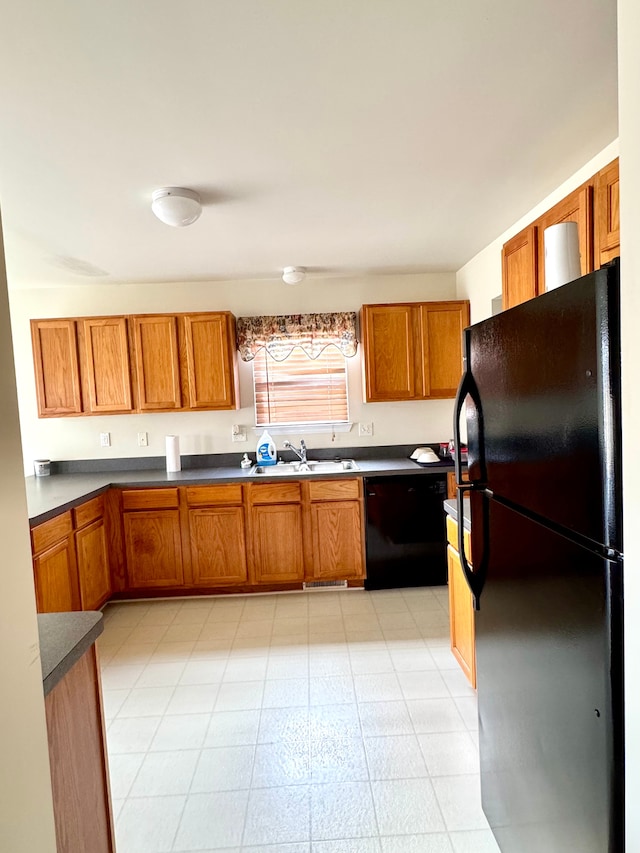 kitchen with dark countertops, light floors, brown cabinetry, black appliances, and a sink