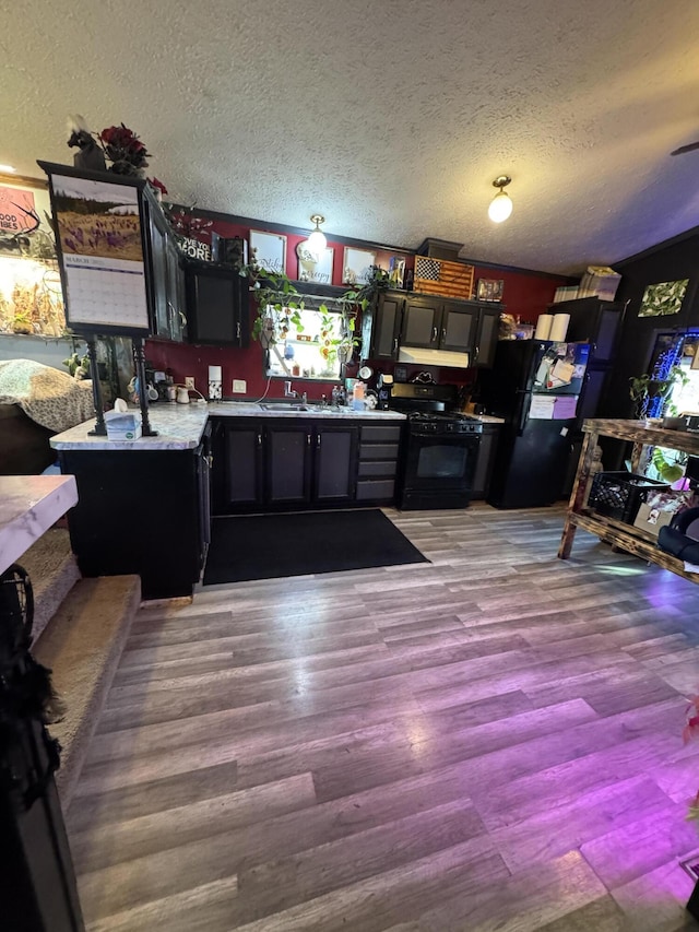 kitchen with a textured ceiling, black appliances, light countertops, and wood finished floors