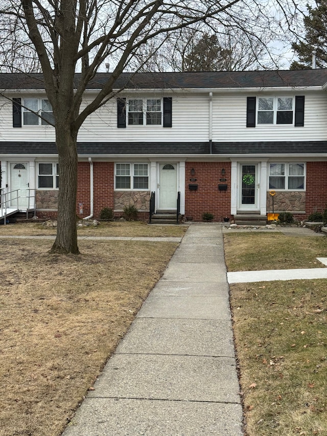 view of property with brick siding, entry steps, and a front lawn