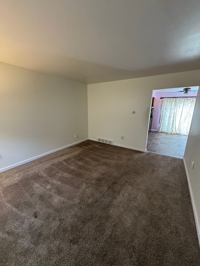 spare room featuring visible vents, baseboards, and dark colored carpet