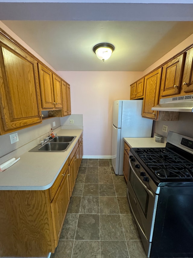 kitchen with brown cabinetry, gas stove, under cabinet range hood, and a sink