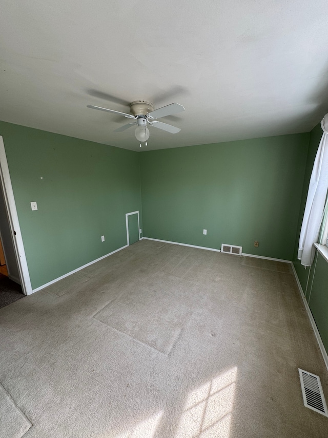 carpeted spare room with visible vents, baseboards, and a ceiling fan