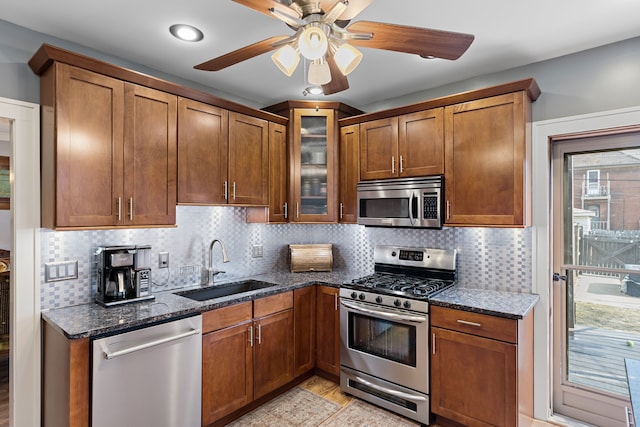 kitchen featuring dark stone countertops, stainless steel appliances, a ceiling fan, and a sink