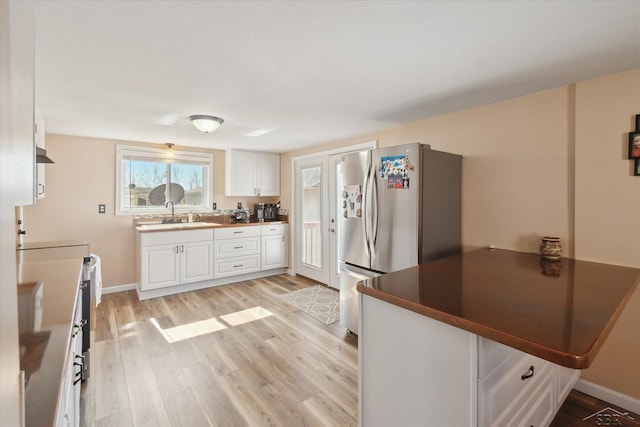 kitchen featuring dark countertops, freestanding refrigerator, light wood-style floors, white cabinetry, and a sink