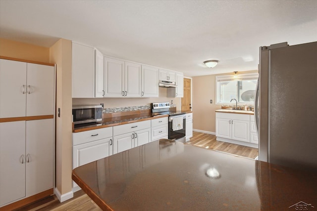 kitchen featuring under cabinet range hood, a sink, stainless steel appliances, white cabinets, and light wood finished floors