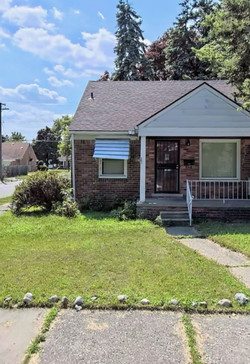 view of front of property with brick siding, covered porch, a front yard, and a shingled roof