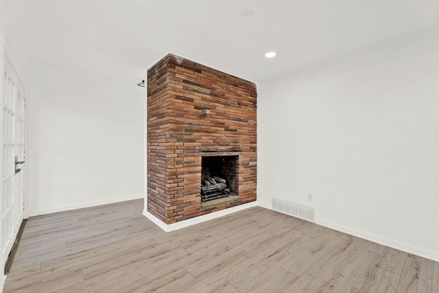 unfurnished living room featuring visible vents, baseboards, a brick fireplace, and wood finished floors