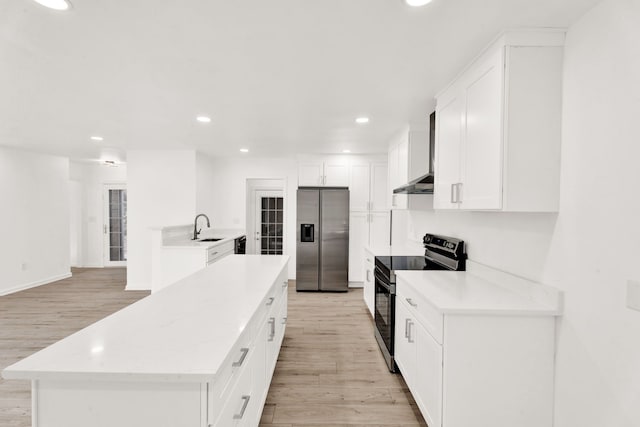 kitchen with a kitchen island, light wood-style flooring, a sink, black appliances, and wall chimney range hood