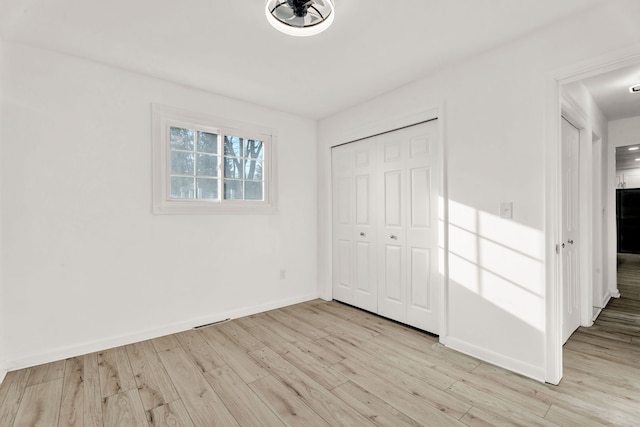 unfurnished bedroom with light wood-type flooring, baseboards, and a closet