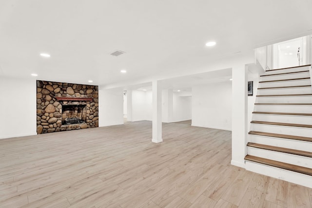 finished below grade area featuring visible vents, stairs, a stone fireplace, recessed lighting, and light wood-style floors