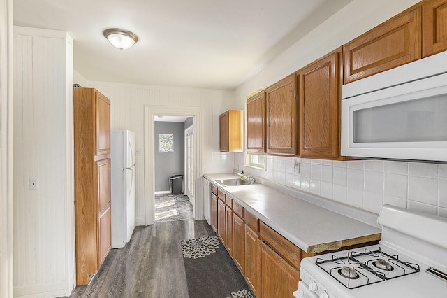 kitchen featuring brown cabinets, a sink, tasteful backsplash, dark wood finished floors, and white appliances