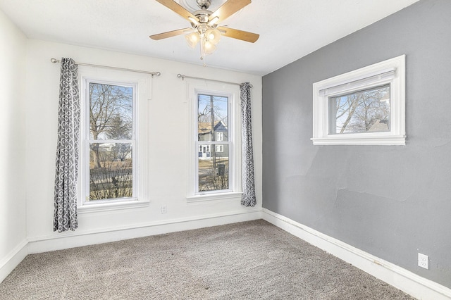 carpeted spare room featuring a wealth of natural light, a ceiling fan, and baseboards