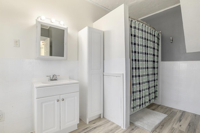 full bath featuring a wainscoted wall, a shower with curtain, wood finished floors, tile walls, and vanity