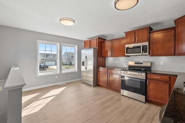 kitchen featuring light wood-style flooring, backsplash, dark stone counters, appliances with stainless steel finishes, and baseboards