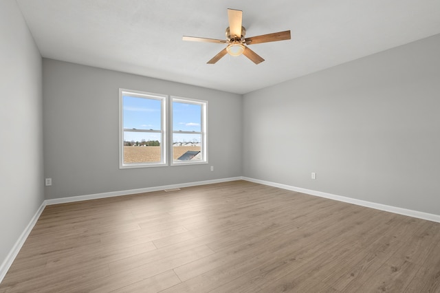 empty room with visible vents, wood finished floors, baseboards, and ceiling fan