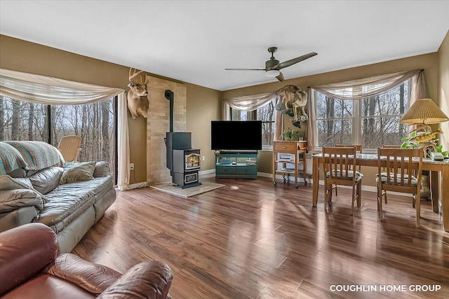 living area featuring baseboards, a wood stove, ceiling fan, and wood finished floors