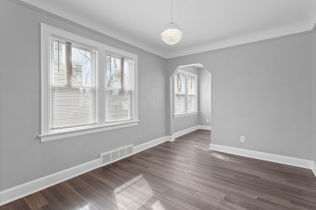 unfurnished room with visible vents, arched walkways, dark wood-type flooring, and baseboards