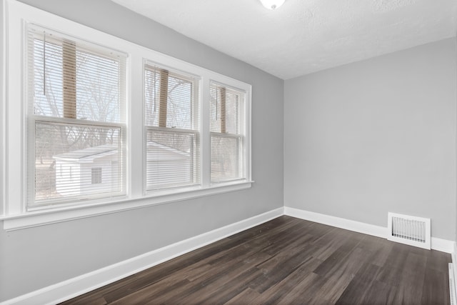 unfurnished room with visible vents, baseboards, dark wood-type flooring, and a textured ceiling