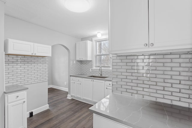 kitchen with tasteful backsplash, a sink, light stone countertops, arched walkways, and dark wood-style flooring