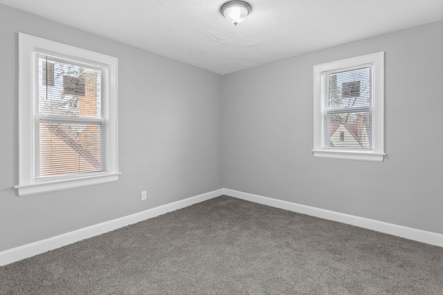 empty room with baseboards, a healthy amount of sunlight, and dark carpet