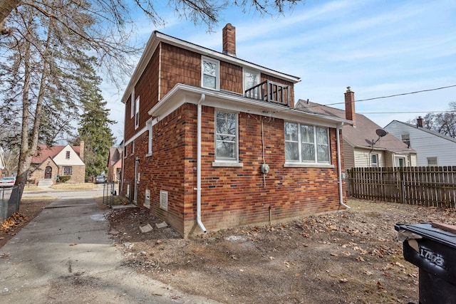 view of home's exterior with brick siding, fence, concrete driveway, a chimney, and a balcony