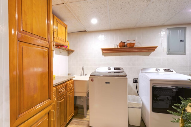 washroom with light wood-type flooring, electric panel, washer and dryer, cabinet space, and tile walls