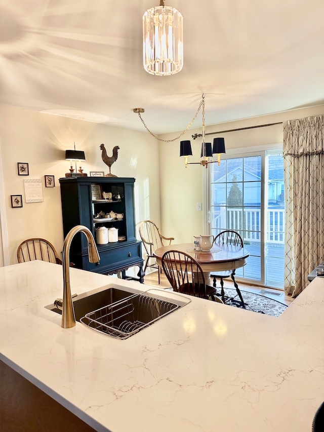 kitchen with a sink, light stone countertops, pendant lighting, and a chandelier