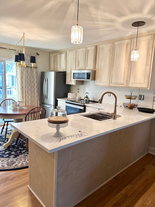 kitchen featuring light brown cabinetry, appliances with stainless steel finishes, a peninsula, light wood-style floors, and a sink