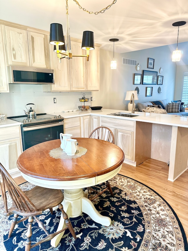 kitchen featuring light wood finished floors, visible vents, a peninsula, stainless steel appliances, and a sink