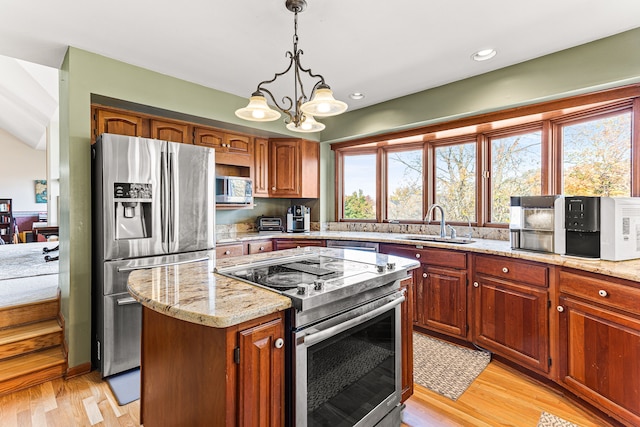 kitchen with a sink, a kitchen island, stainless steel appliances, light wood finished floors, and light stone countertops