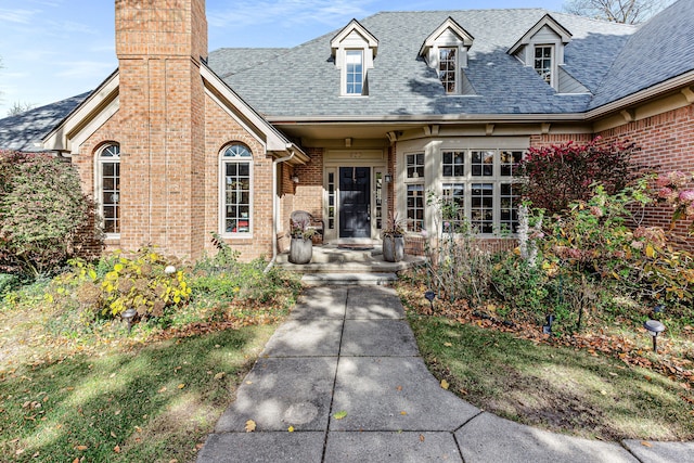 view of exterior entry featuring brick siding, roof with shingles, and a chimney