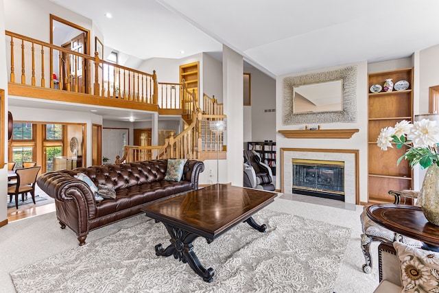 living area with visible vents, a tiled fireplace, stairway, built in features, and vaulted ceiling