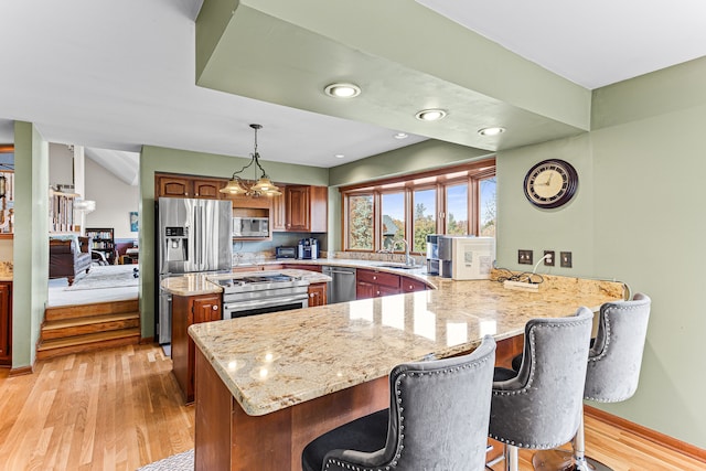 kitchen featuring a sink, light stone counters, stainless steel appliances, a peninsula, and light wood finished floors