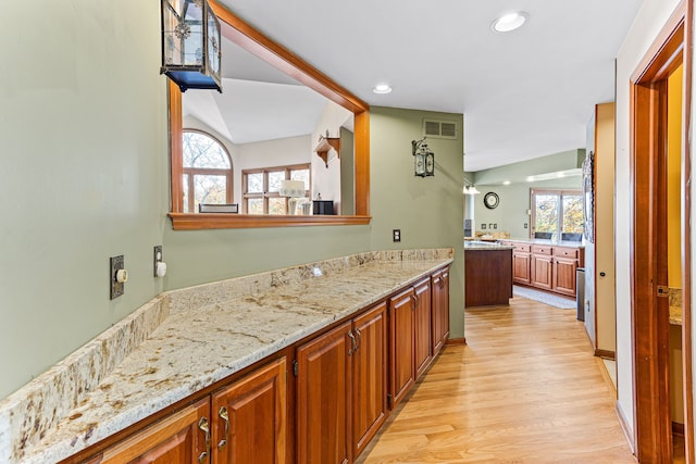 kitchen with light wood finished floors, visible vents, light stone countertops, recessed lighting, and brown cabinets