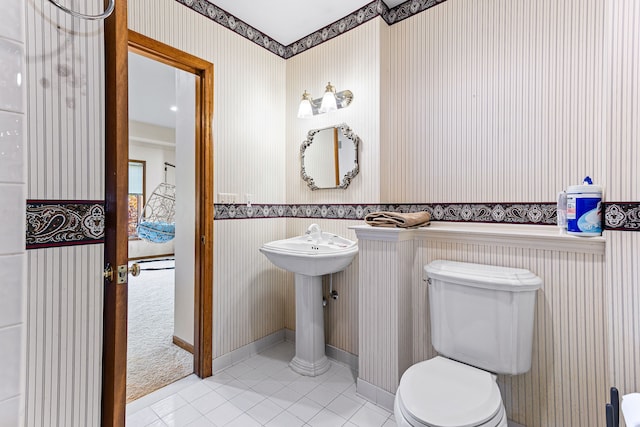 half bath with tile patterned floors, toilet, and wallpapered walls