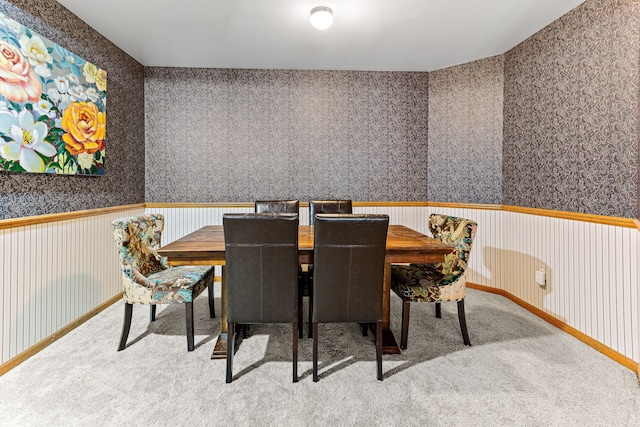 carpeted dining area with wainscoting and wallpapered walls