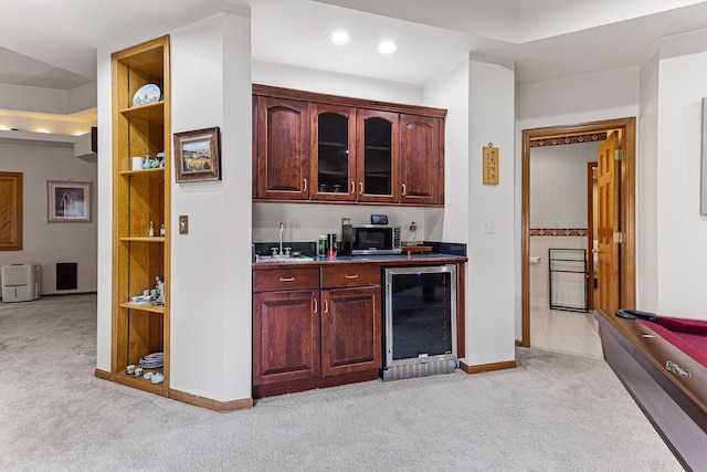 bar with light carpet, beverage cooler, a sink, stainless steel microwave, and baseboards