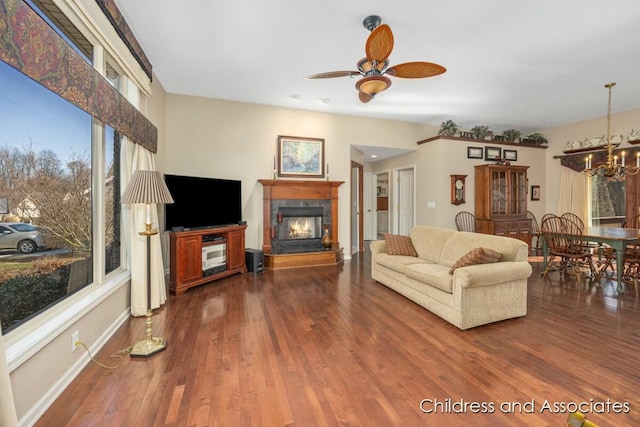 living room featuring a glass covered fireplace, ceiling fan with notable chandelier, baseboards, and wood finished floors