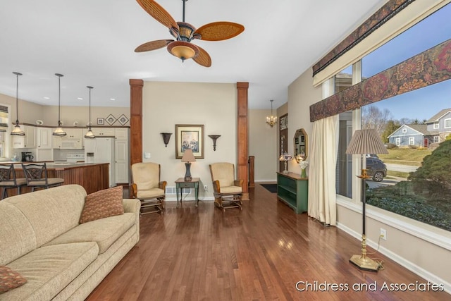 living area featuring baseboards, dark wood-style floors, and ceiling fan with notable chandelier